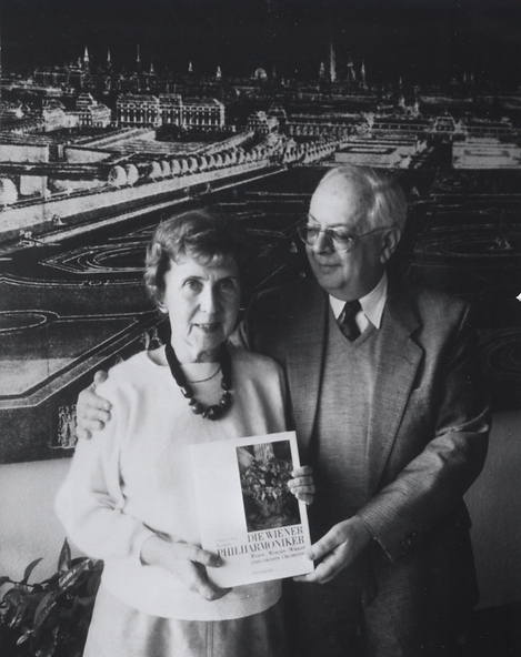 Sie sehen eine Schwarz-Weiß-Fotographie, auf der Herta und Kurt Blaukopf ihr Buch "Die Wiener Philharmoniker" präsentierend in die Kamera halten. Herta Blaukopf blickt dabei in die Kamera, während Kurt Blaukopf seinen Arm um sie gelegt hat und zu ihr hinüber sieht.